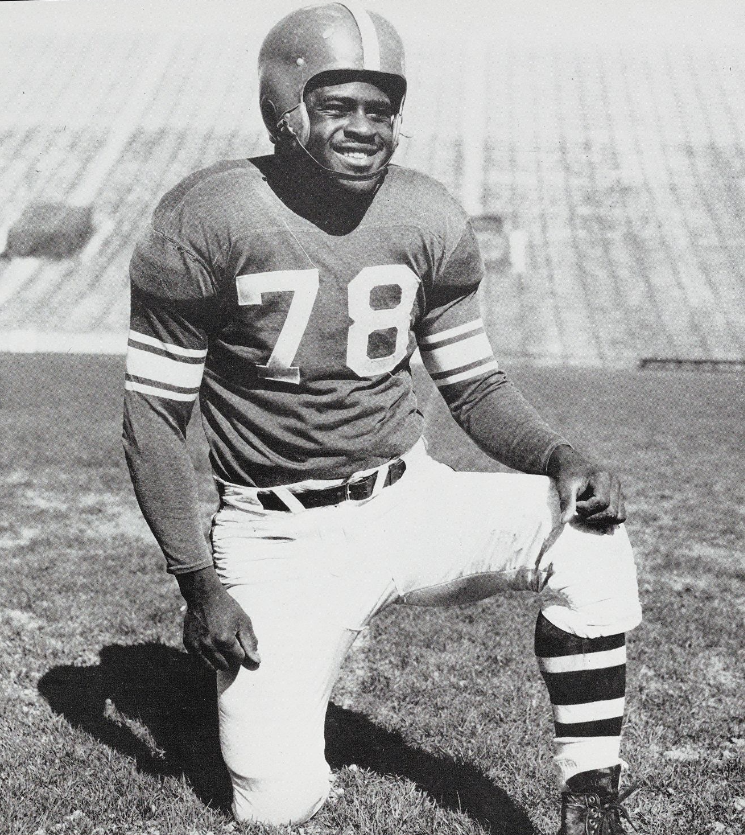 Vintage black and white image of Don Coleman (offensive tackle) in his Michigan State football uniform and helmet on a pose on one knee