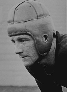 Vintage black and white head shot image of Elmer Layden in 1923 wearing a leather helmet and Notre Dame football uniform, hunched down appearing to ready for a play to start