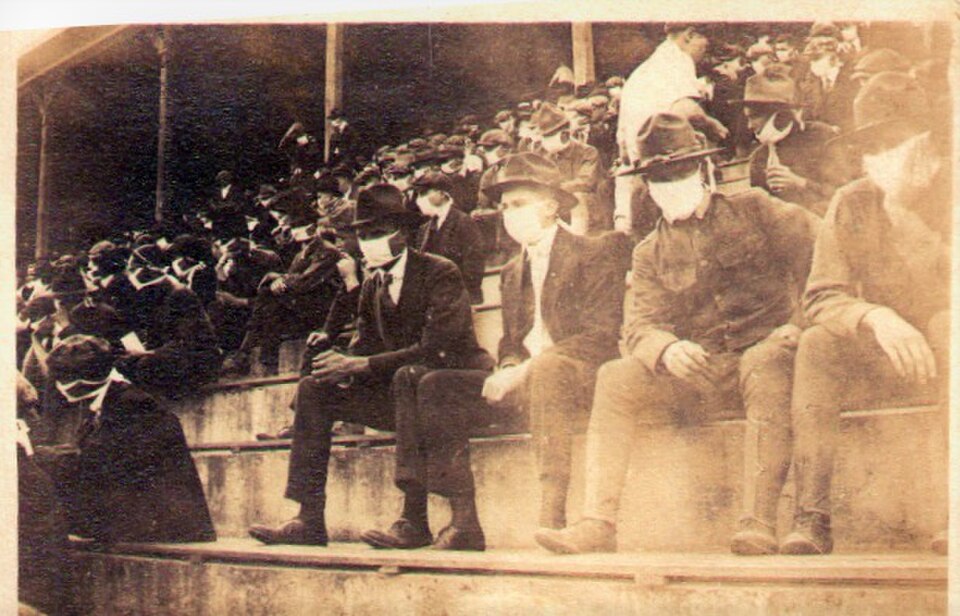 Vintage black and white image of Photo of the crowd at an undetermined 1918 Georgia Tech home football game. Almost everyone in the crowd is wearing face masks due to the Spanish flu pandemic.