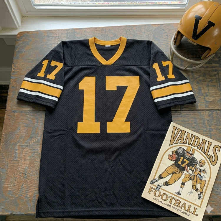 Vintage University of Idaho Vandals #17 football jersey. Black mesh with gold block numbers and gold-and-white striped sleeves. Features a gold 'V' helmet and a vintage Vandals football program for historical Big Sky Conference research and Pigskin Dispatch archives