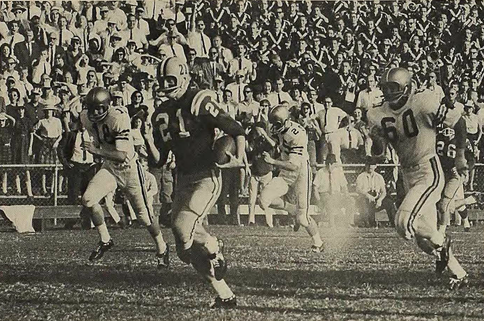 SEO Optimized Alt Text "Vintage 1962 black-and-white game action photograph featuring LSU Tigers halfback Jerry Stovall (#21) breaking away down the sideline. Stovall carries the football in a dark jersey with white block numbers and a striped helmet with a single-bar facemask, pursued by defenders in light jerseys numbered 18 and 60, with a packed stadium crowd in the background. A primary source for SEC football history and Pigskin Dispatch archives.