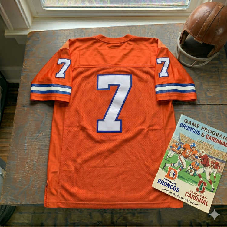 Vintage Denver Broncos #7 football jersey. Orange mesh with white and royal blue shadowed block numbers and striped sleeves. Features a Denver Broncos vs. Stanford Cardinal game program and a vintage leather helmet for historical NFL and John Elway research for Pigskin Dispatch archives.