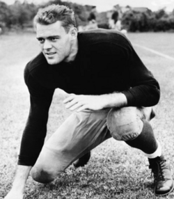 Promotional black and white image of Larry Kelley in full Yale football gear (minus helmet) in a three point stance pose.