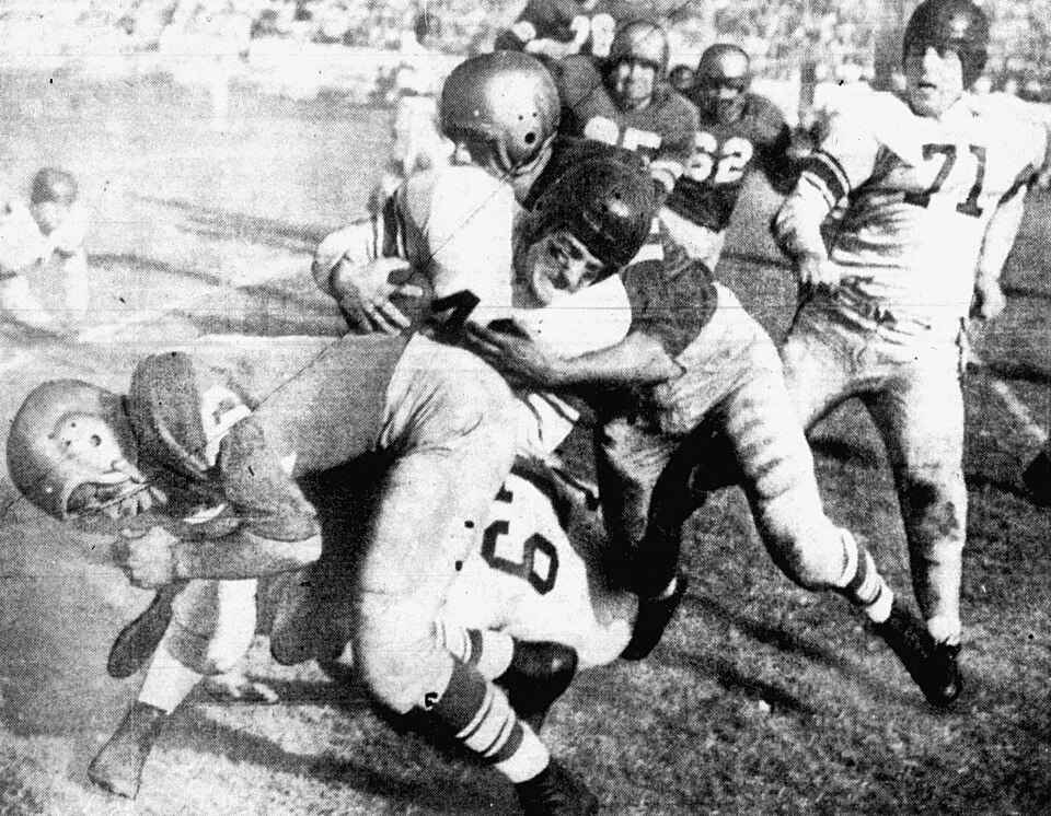 Vintage black and white game action photo of Loyola Lions defensive end Gene Brito (foreground) makes the tackle on Santa Clara Bronchos back Jack Kaplan (with ball) during a game on November 26, 1950 at Gilmore Field in Los Angeles, California.