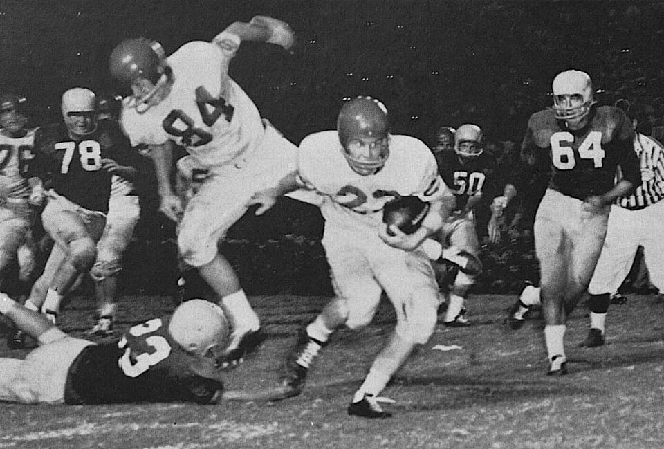 Black and white game action photo of An American football game between the 1957 Houston Cougars football team and the Miami Hurricanes at Rice Stadium in Houston. Pictured are Houston's Claude King (#22), Bob Borah (#84), and Charlie Brown (#76), and Miami's Dan Coughlin (#64), Byron Blasko (#23), Frank Nodoline (#78), and Jim Otto (#50). 1958 Houstonian photography staff.