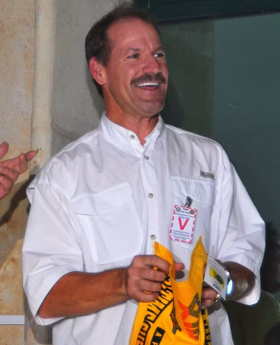 Color photo of Bill Cowher in a white button down shirt holding a yellow Terrible Towel