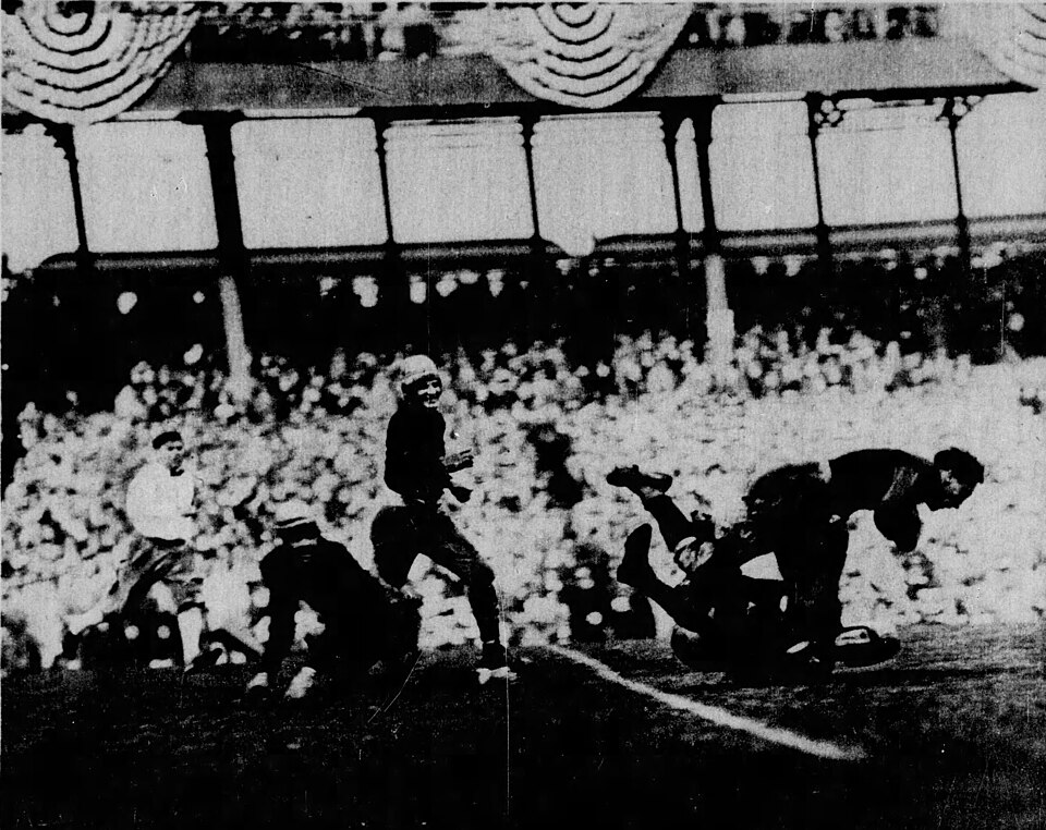 Vintage black and white newspaper game action photo of Notre Dame vs. Army football at Polo Grounds on October 18, 1924. Caption into Chicago Tribune (published on November 2, 1924): "How it's done- Noth escapes the camea man nowadays on the football field. This fleet snap-shop reigsters instructively an exciting moment in the recent New York game between Army and Notre Dame, with a Notre Dame player, carying the ball, being tackled by a plunging warrior of the Army. The westerners won this time, 13 to 7"