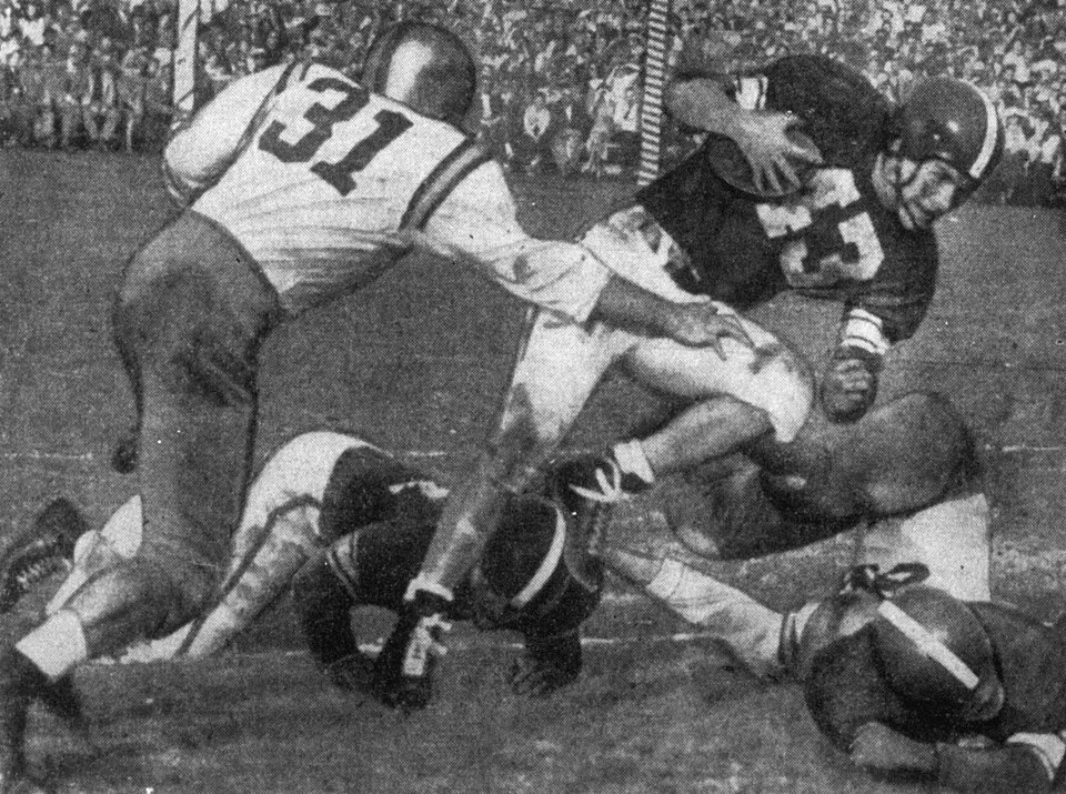 Vintage black and white newspaper game action photo of UCLA Bruins player Pete Dailey (number 31, left) tackles Michigan State Spartans quarterback John Matsock during the second quarter of the Rose Bowl on January 1, 1954 in Pasadena, California.
