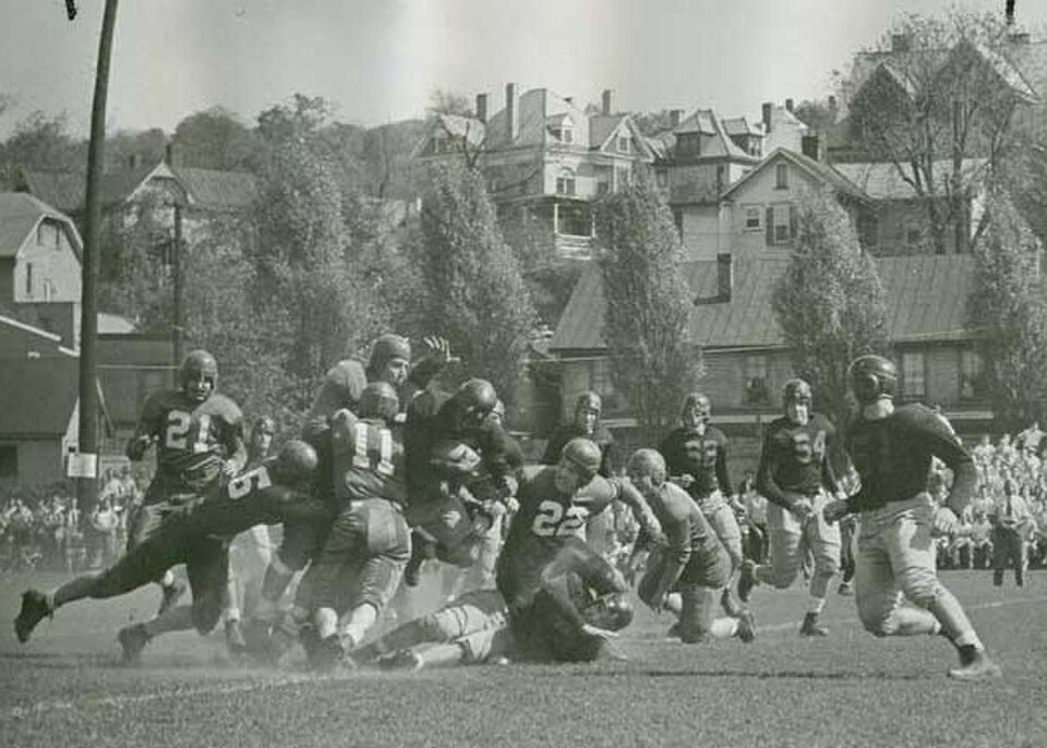 Vintage 1946 action photograph of the Washington & Jefferson Presidents football team at College Field. Heavy line collision features players in leather helmets and block number jerseys #21, #11, and #22. Historic houses line the hillside in the background of this primary source for post-war Pennsylvania college football and Pigskin Dispatch archives.