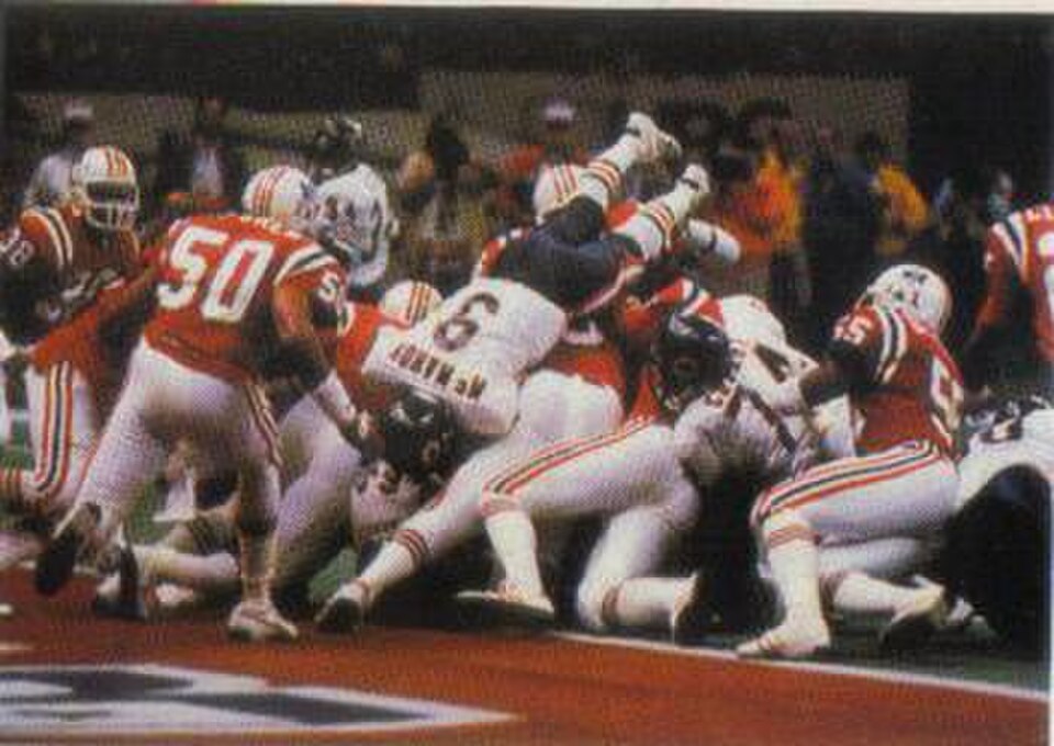 A full color football card from the 1986 Jeno's Pizza NFL football card stickers set of Chicago Bears quarterback Jim McMahon rushing the ball for a touchdown against the New England Patriots in Super Bowl XX. The card is numbered #11 in the set.