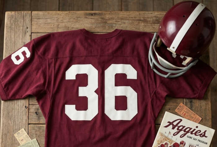 AI created crimson Texas A&M jersey and helmet from the 1960s era with number 36 on it lying on an old wooden table next to a representative 1960s game day program.