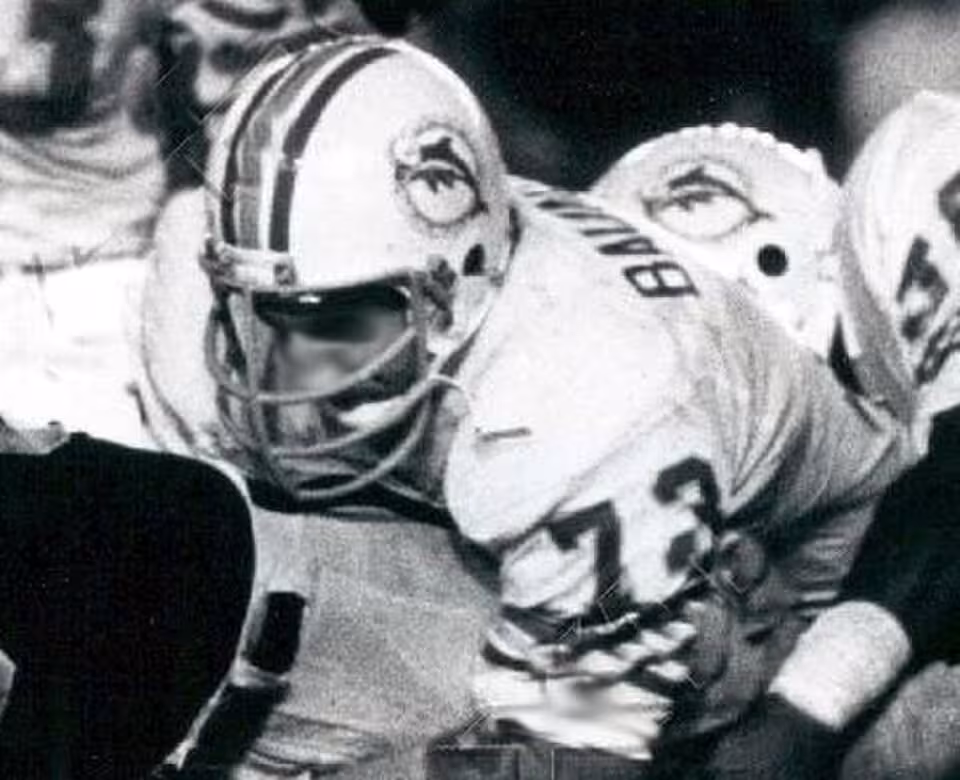 A black and white game action cropped photo fo Miami Dolphins defensive tackle Bob Baumhower tackling Oakland Raiders running back Mark van Eeghen during an October 8, 1979 game at Oakland–Alameda County Coliseum.