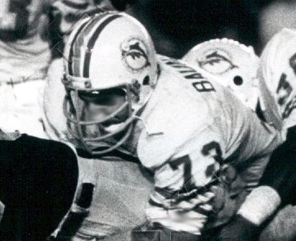 A black and white game action cropped photo fo Miami Dolphins defensive tackle Bob Baumhower tackling Oakland Raiders running back Mark van Eeghen during an October 8, 1979 game at Oakland–Alameda County Coliseum.
