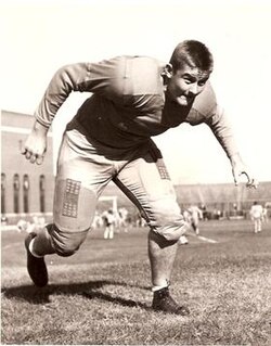 Vintage black and white publicity photo of a full body Clayton Tonnemaker, in Monnesota Gophers football uniform minus helmet, in an action pose.