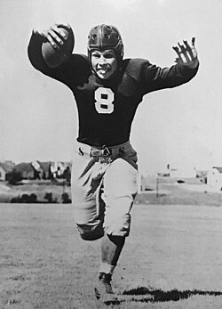 Black and white whimsical full body pose of O'Brien with TCU in 1938 in his football uniform, tongue out in a pose.