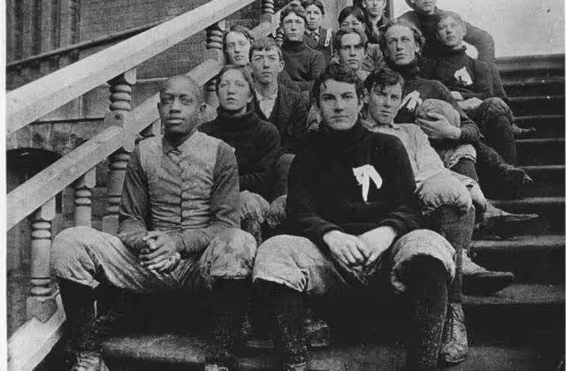 Vintage black and white image of a late nuneteenth century American football high school integrated team posing for a photo on some prominent cement steps.