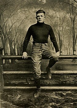 Vintage black and white publicity full body image of H. H. Ketcham of Yakle in full football uniform sitting on the famous Yale Fence.