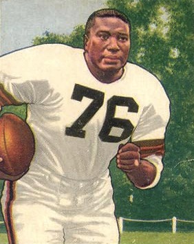Full color image of Marion Motley, American football fullback, on a 1950 Bowman football card in his all white Cleveland Browns uniform posing without a helmet and carrying a football.