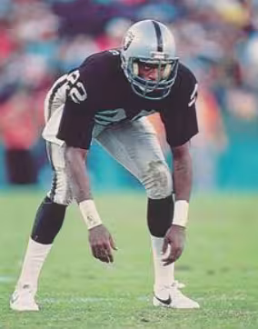 Full color game day image of Mike Hayes wit the LA Raiders in 1985 in full iniform with black number 22 jersey