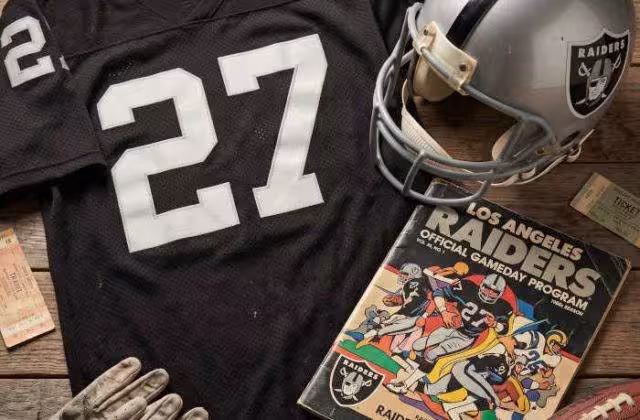 AI-generated black jersey 27 on a wooden table with a silver Raiders helmet and period example of a program