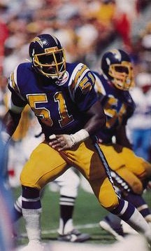 Full color game action image in the public domain of Wikimedia Commons of Woodrow Lowe playing for the San Diego Chargers in 1984. Image taken from a trading card released in 1985. The 25th anniversary patch over the player's left chest identifies the season as 1984.