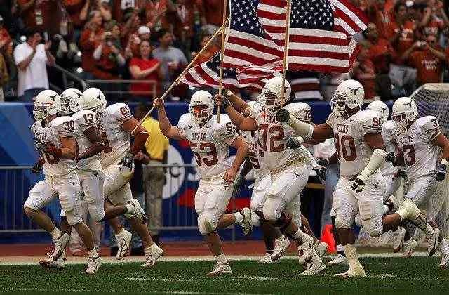 Full color photo of white clad University of Texas Longhorns football players enter the field for the 2005 Bix XI Championship Game., one carrying an American flag KeithJJ on Pixabay