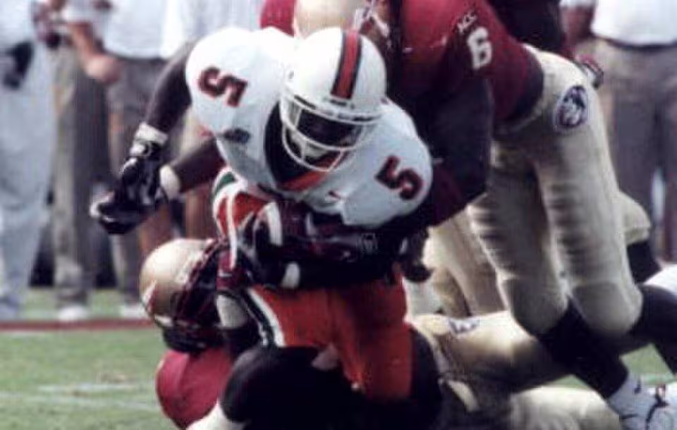Full color game action photo of Miami Hurricanes running back Edgerrin James being tackled by an Florida State Seminoles defenders Derrick Gibson (6) and an unidentified player at Doak Campbell Stadium - Tallahassee, Florida