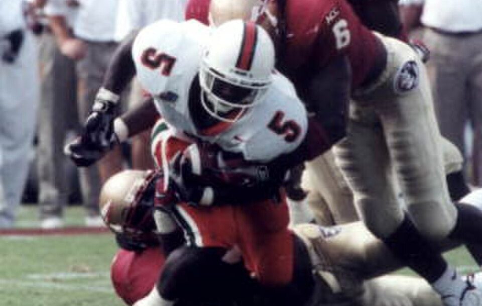 Full color game action photo of Miami Hurricanes running back Edgerrin James being tackled by an Florida State Seminoles defenders Derrick Gibson (6) and an unidentified player at Doak Campbell Stadium - Tallahassee, Florida