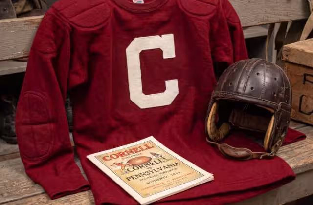 Gemini AI generated image of a 1913 era red American football jersey, without a name on it, and a matching period-correct helmet, the program cover appropriate to the era and team.
