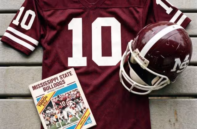 AI-generated crimson jersey 10 on a wooden table with a crimson "M" helmet and period example of a program
