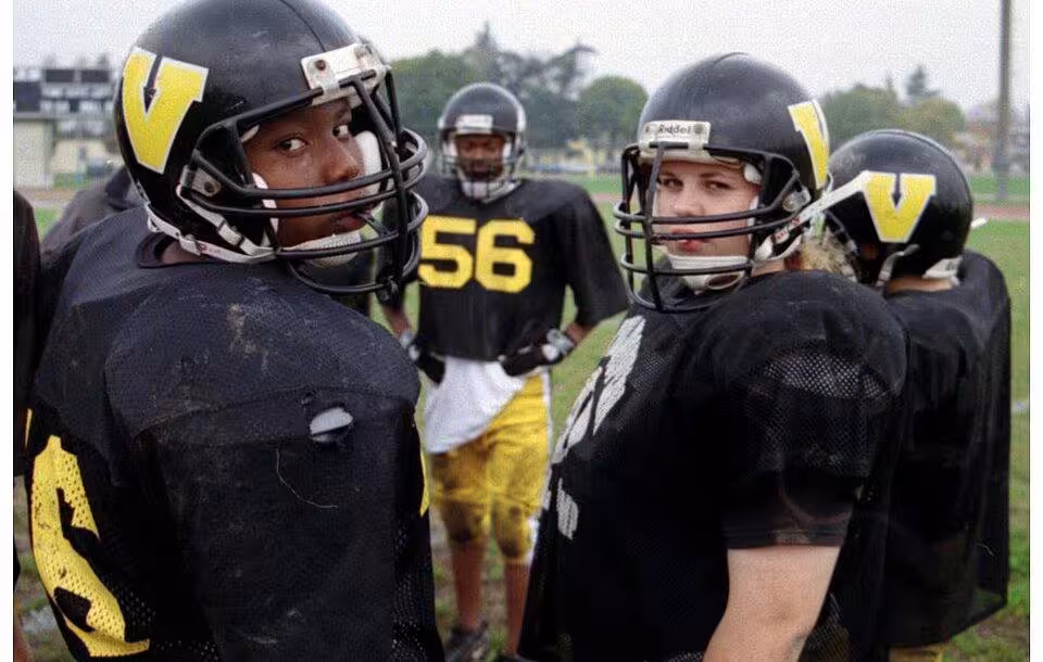 Color image photo of U.S. Department of Defense Dependents Schools (DoDDS) sponsor a wide range of sports activities for its students. Vicenza American High School students at football practice on Caserma Ederle, Italy (October 2002). The team featured a female center (pictured right). Photo by Peter Rimar.
