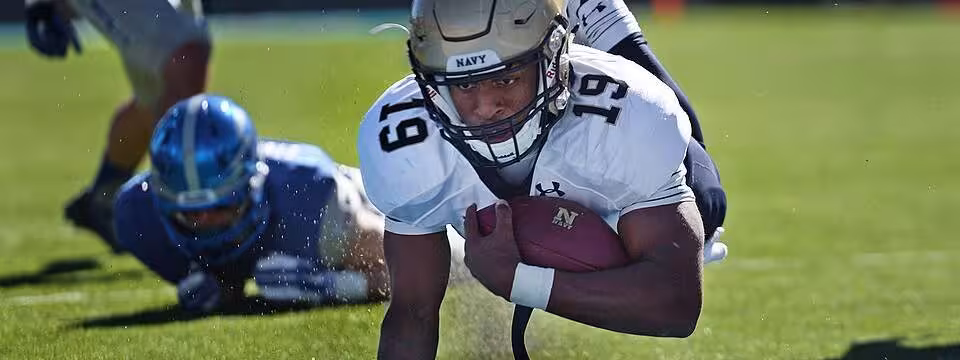 Full color game action photo of Navy quarterback Keenan Reynolds lands in the end zone for a touchdown against Air Force at the Air Force Academy in Colorado Springs, Colo. Oct. 4, 2014. Air Force won the game, which honored the athletes in the 2014 Warrior Games. (DoD News photo by EJ Hersom)
