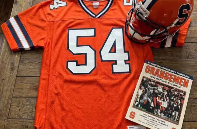 Gemini AI-created image of a 1992-era Syracuse American football jersey 54, without a name on it, and a matching period-correct helmet, the program cover appropriate to the era and team.