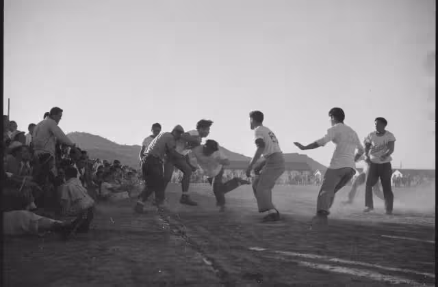 The full caption for this photograph reads: Gila River Relocation Center, Rivers, Arizona. A rousing game of football was played at this center between the Vandals and the Leather Necks on Thanksgiving day. The Vandals won 18 to 6.