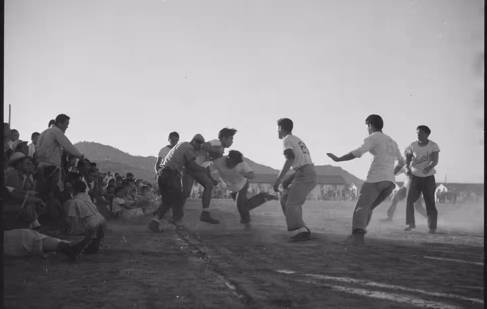 The full caption for this photograph reads: Gila River Relocation Center, Rivers, Arizona. A rousing game of football was played at this center between the Vandals and the Leather Necks on Thanksgiving day. The Vandals won 18 to 6.