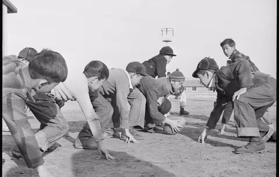 Black and white image, Granada Relocation Center, Amache, Colorado. Grade school boys playing touch football during the recess play period.Courtesy of Wikimedia Commons uploader, Tom Parker.