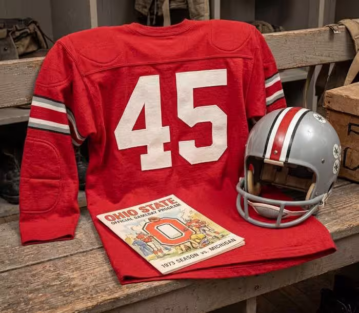 Gemini AI-created image of a 1973-era Ohio State University American football jersey 45, without a name on it, and a matching period-correct helmet, the program cover appropriate to the era and team.