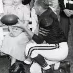 Black and white publicity photo of The original caption describes the photograph as: Military Personnel with Some of the Members of the Chicago Bears Football Team - In the group are George Blande, Cpl Jo Ruff, Cpl Sonia Schmit, Harry Jagade, fullback of the Bears, Larry Brink, and Pfc John Carbon.