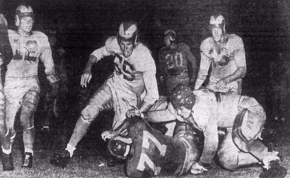 Game action photo of Vitamin Smith (bottom center, number 77) is tackled after a ten yard gain by Bob Levenhagen (bottom right) and Bobby Thompson (center, number 65) during an intrasquad game at Gilmore Stadium in Los Angeles, California on August 17, 1949.