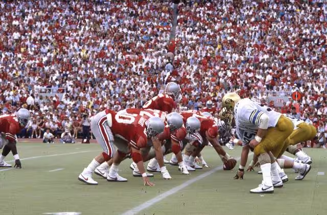 A view from the field in a packed Ohio Stadium as the Ohio State Buckeyes play the Colorado Buffaloes. The Buckeyes won the football game 13-10, in front of a crowd of 88,404 spectators. This photograph features the Buckeye offense on the field led by Jim Karsatos, #16, at quarterback. Sept 20, 1986.