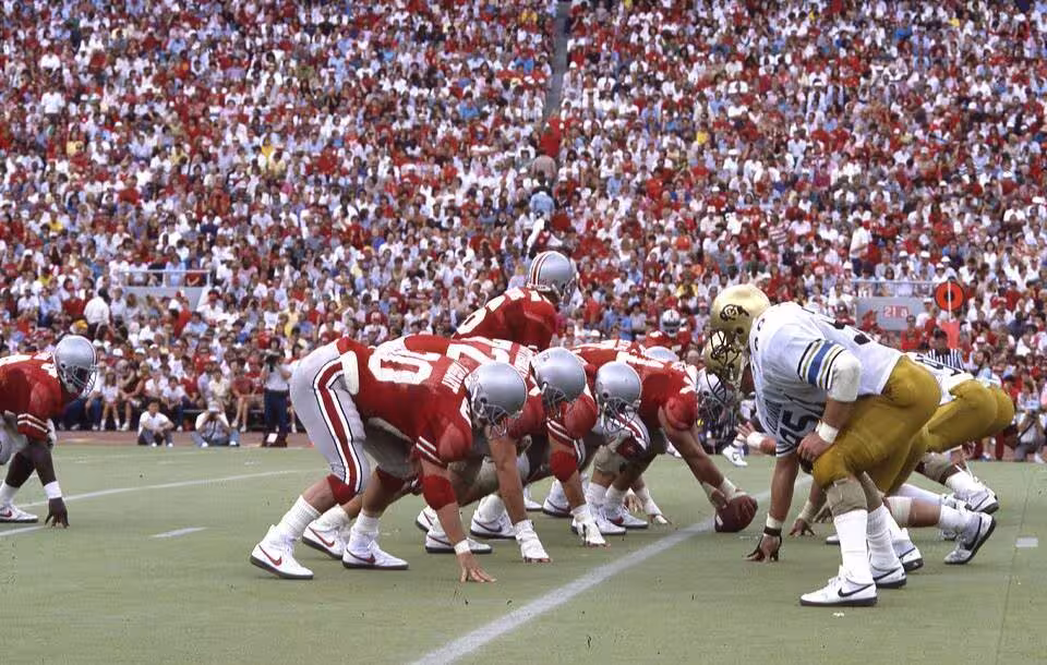 A view from the field in a packed Ohio Stadium as the Ohio State Buckeyes play the Colorado Buffaloes. The Buckeyes won the football game 13-10, in front of a crowd of 88,404 spectators. This photograph features the Buckeye offense on the field led by Jim Karsatos, #16, at quarterback. Sept 20, 1986.