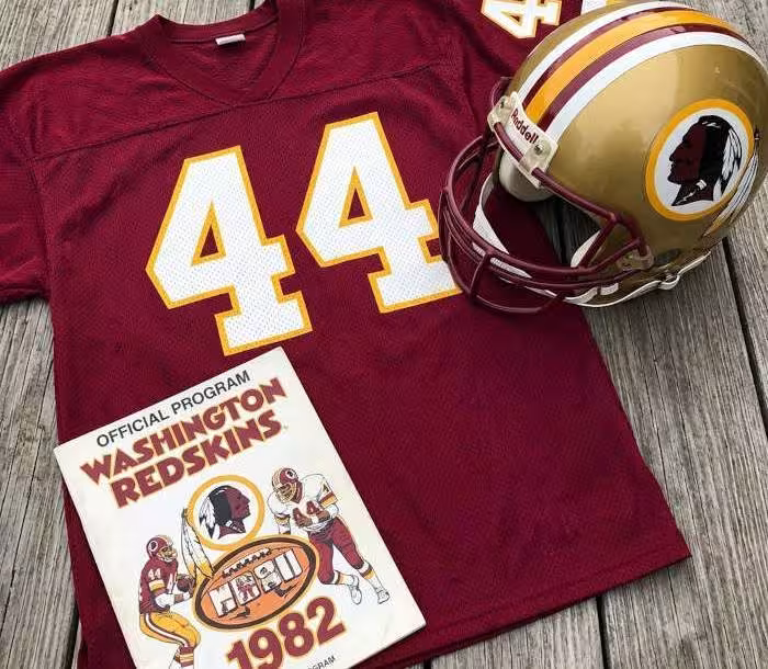 Gemini AI generated image of a 1980s-era red American football jersey 44, without a name on it, and a matching period-correct helmet, the program cover appropriate to the era and team.