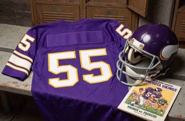 Gemini AI-created image of a 1982-era Minnesota NFL American football jersey 55, without a name on it, and a matching period-correct helmet, the program cover appropriate to the era and team.