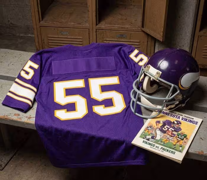 Gemini AI-created image of a 1982-era Minnesota NFL American football jersey 55, without a name on it, and a matching period-correct helmet, the program cover appropriate to the era and team.
