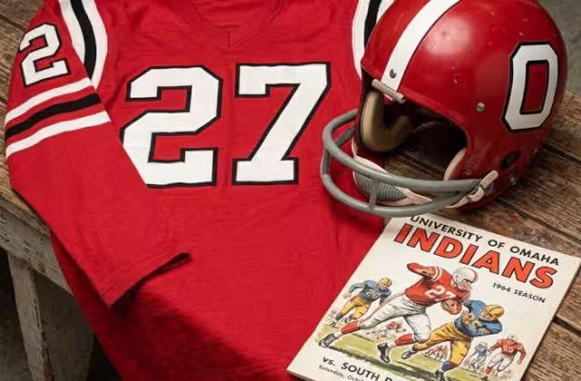 Gemini AI-created image of a 1964-era Nebraska Omaha American football jersey 27, without a name on it, and a matching period-correct helmet, the program cover appropriate to the era and team.