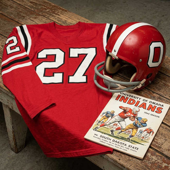 Gemini AI-created image of a 1964-era Nebraska Omaha American football jersey 27, without a name on it, and a matching period-correct helmet, the program cover appropriate to the era and team.