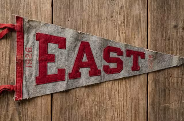 Here is a photograph of a gray and scarlet "EAST" pennant from 1926, designed to look like an authentic wool-felt relic from the era with natural aging, frayed edges, and period-specific typography.