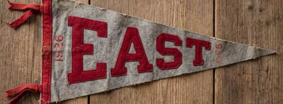Here is a photograph of a gray and scarlet "EAST" pennant from 1926, designed to look like an authentic wool-felt relic from the era with natural aging, frayed edges, and period-specific typography.