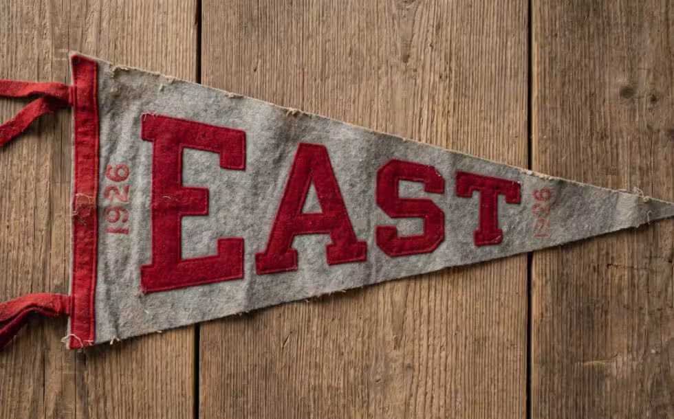 Here is a photograph of a gray and scarlet "EAST" pennant from 1926, designed to look like an authentic wool-felt relic from the era with natural aging, frayed edges, and period-specific typography.